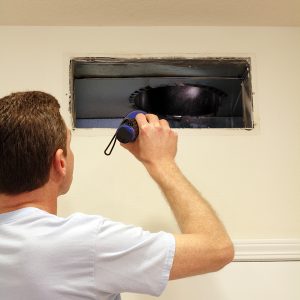 Adult male shining a flashlight into an air duct return vent to check for any need of cleaning dust or any other maintenance.